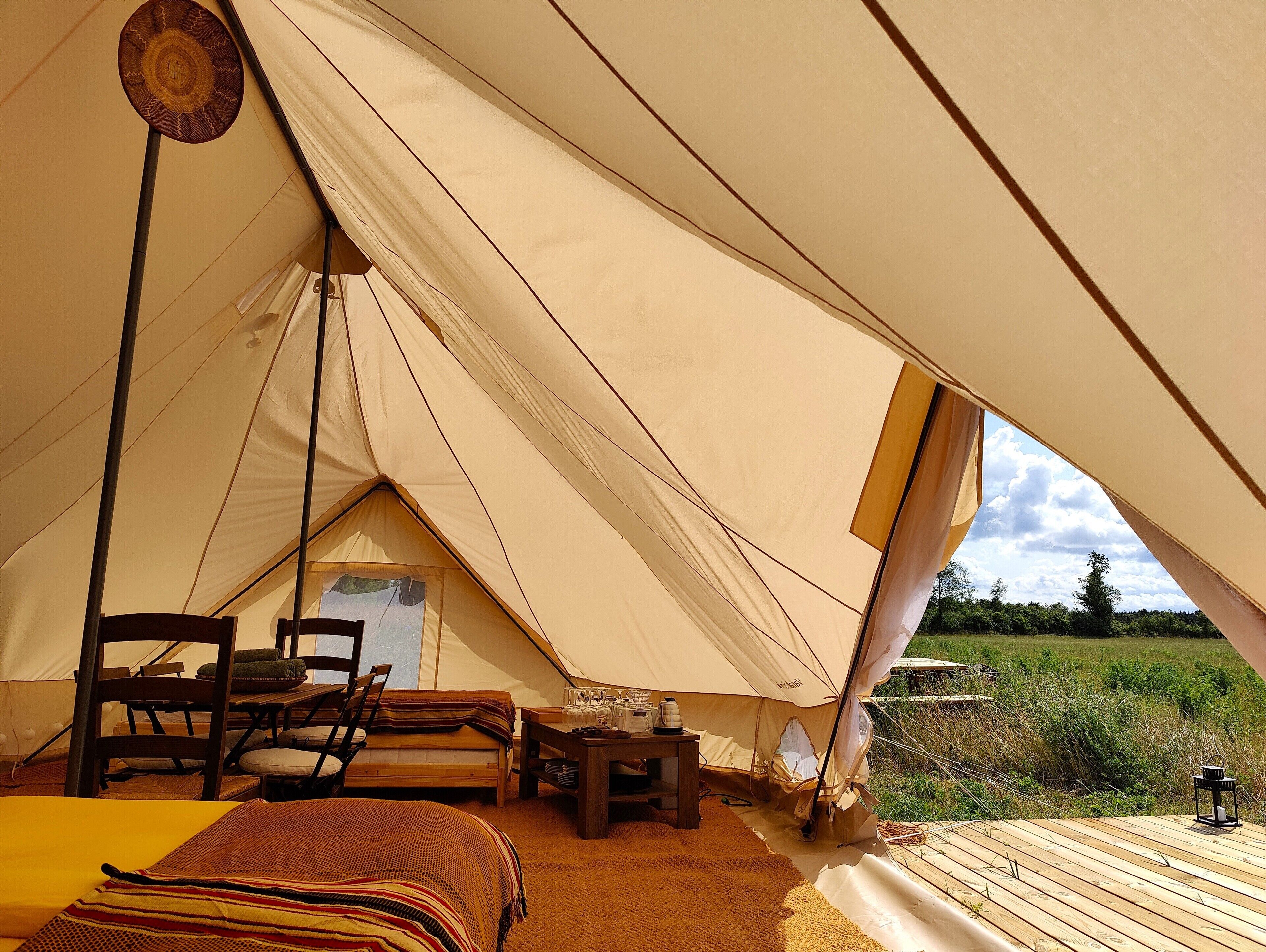 A tent with a bed, chairs, a table with glasses, and a view of the outdoors.