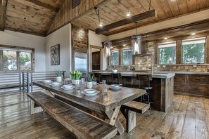 A rustic kitchen with a wooden table, stone backsplash, and hanging pendant lights.