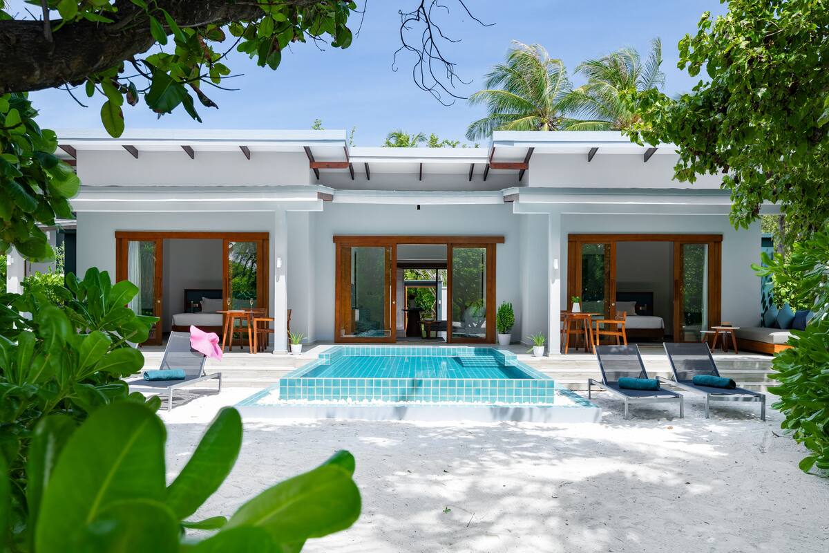 A modern resort with a swimming pool, sun loungers, and a covered outdoor seating area.