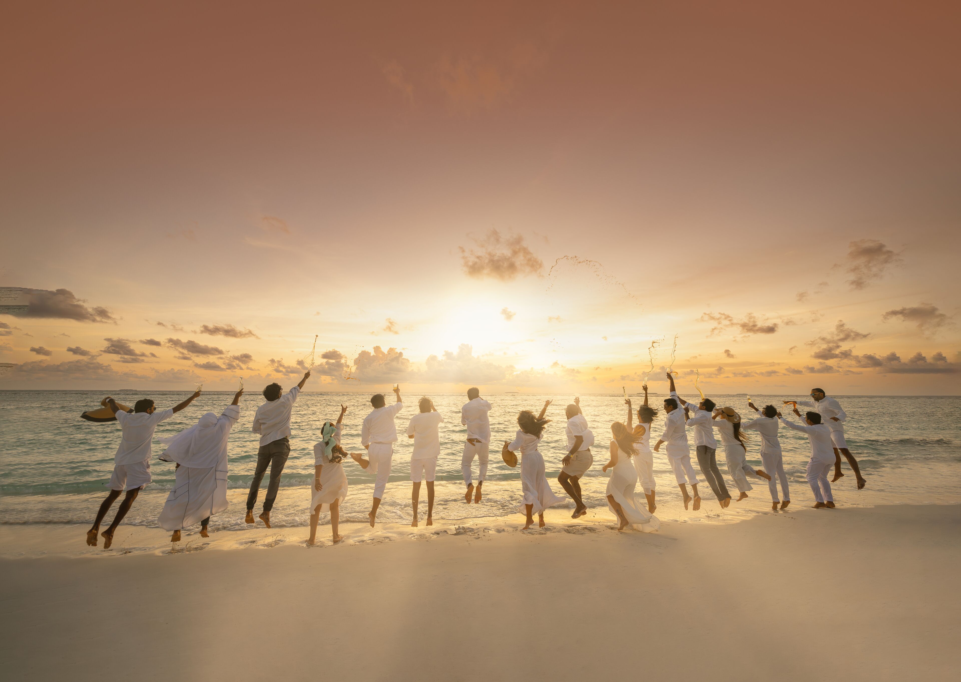 A group of people in white attire dancing on a beach at sunset.