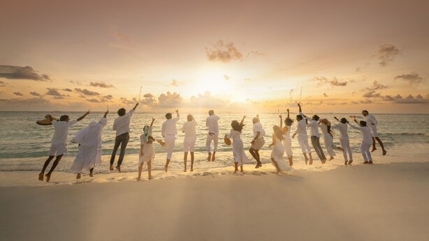 Un grupo de personas vestidas de blanco bailando en la playa al atardecer.