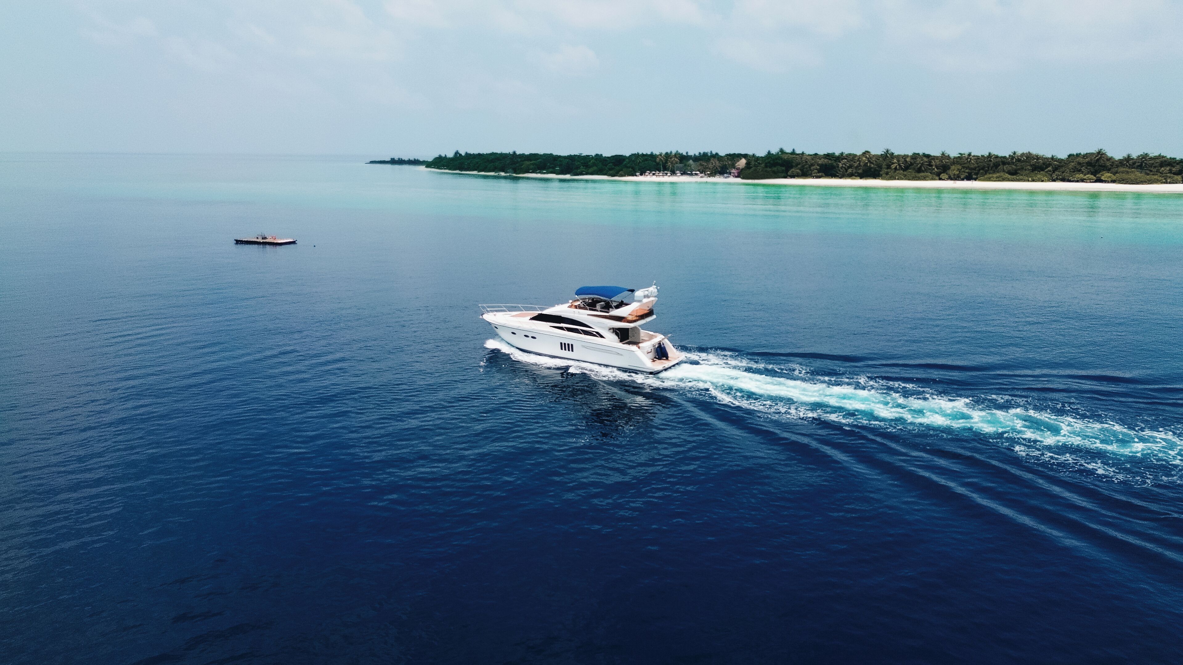 A yacht cruising on a calm sea with a beach and palm trees in the background.
