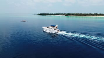 A yacht cruising on a calm sea with a beach and palm trees in the background.