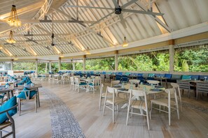 A spacious outdoor dining area with multiple tables and chairs, a covered roof, and a view of lush greenery. -  Ifuru Island Maldives  (Ifuru)