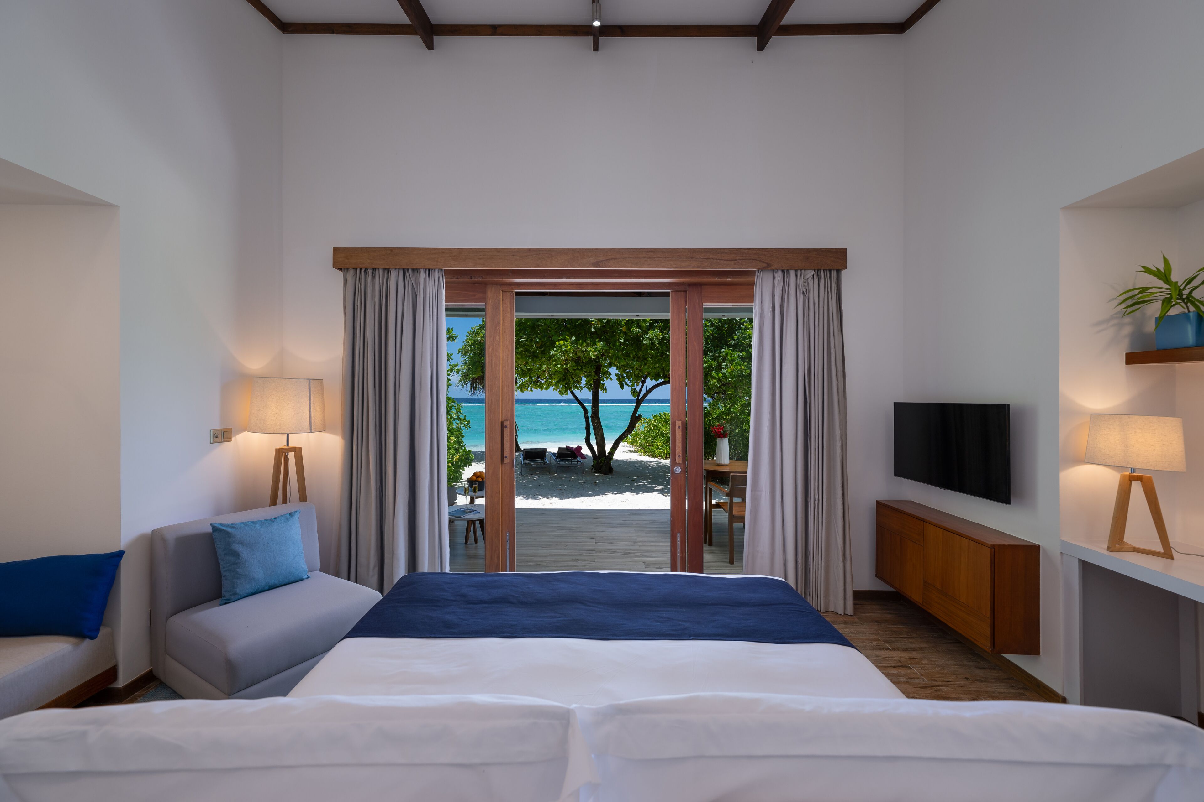 A hotel room with a bed, a sofa, a TV, and a view of the beach.