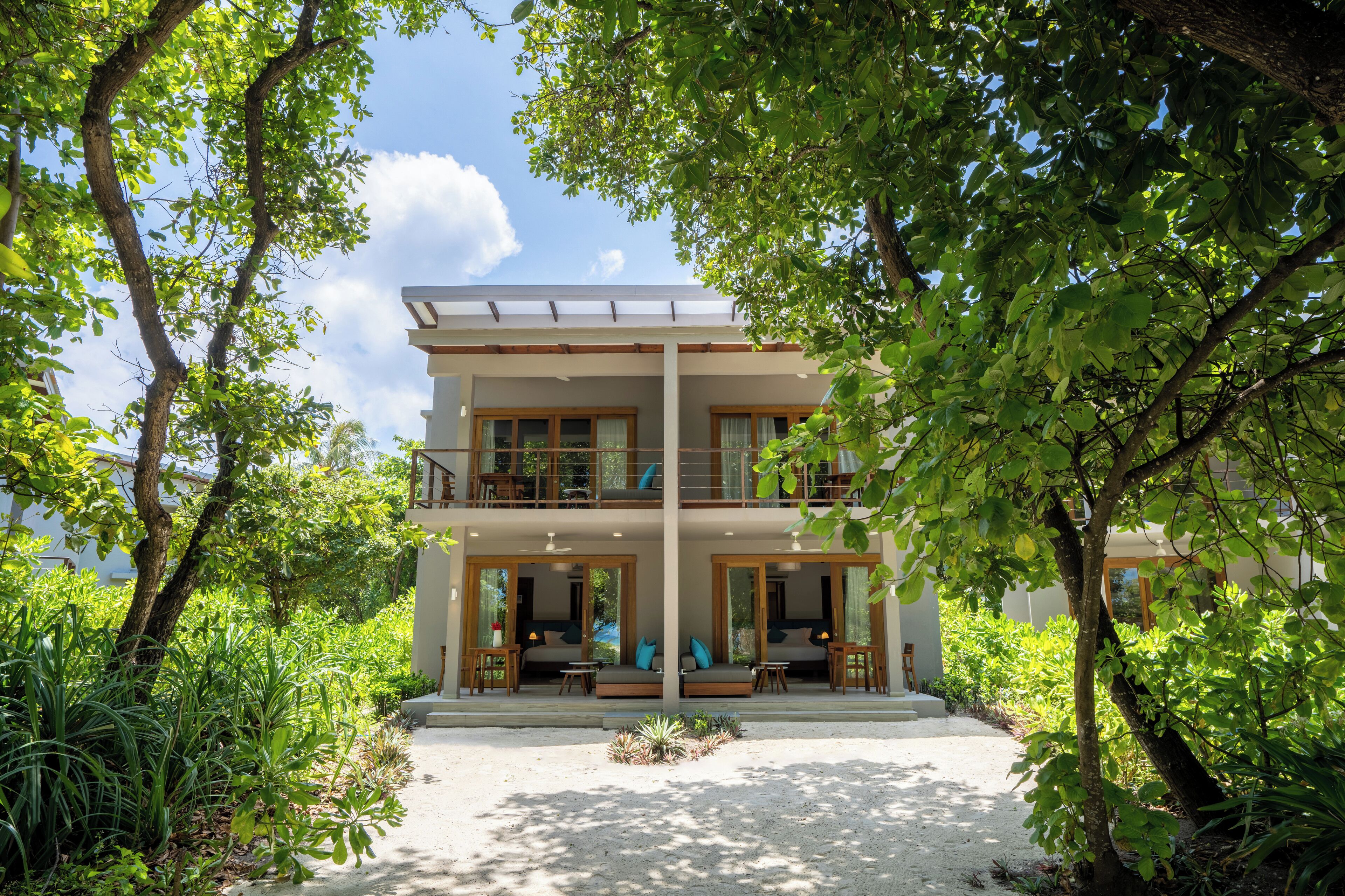 A two-story building with a covered balcony, surrounded by lush greenery.
