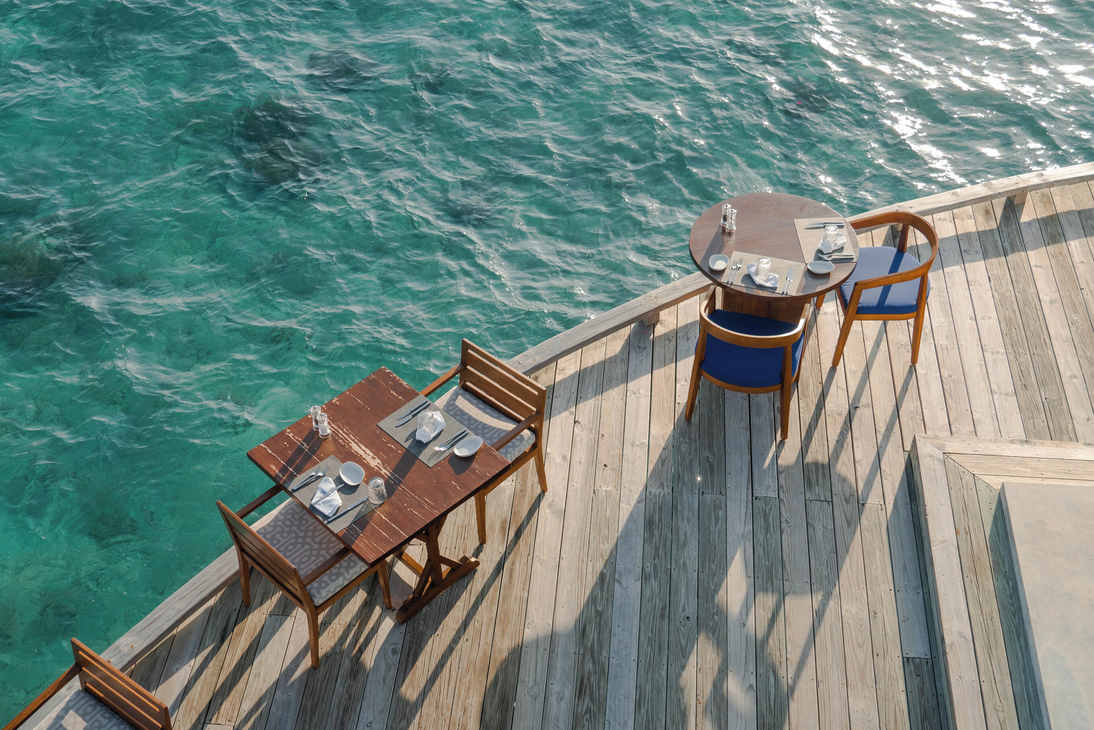 Una terraza de madera con una mesa y sillas que da a aguas turquesas.