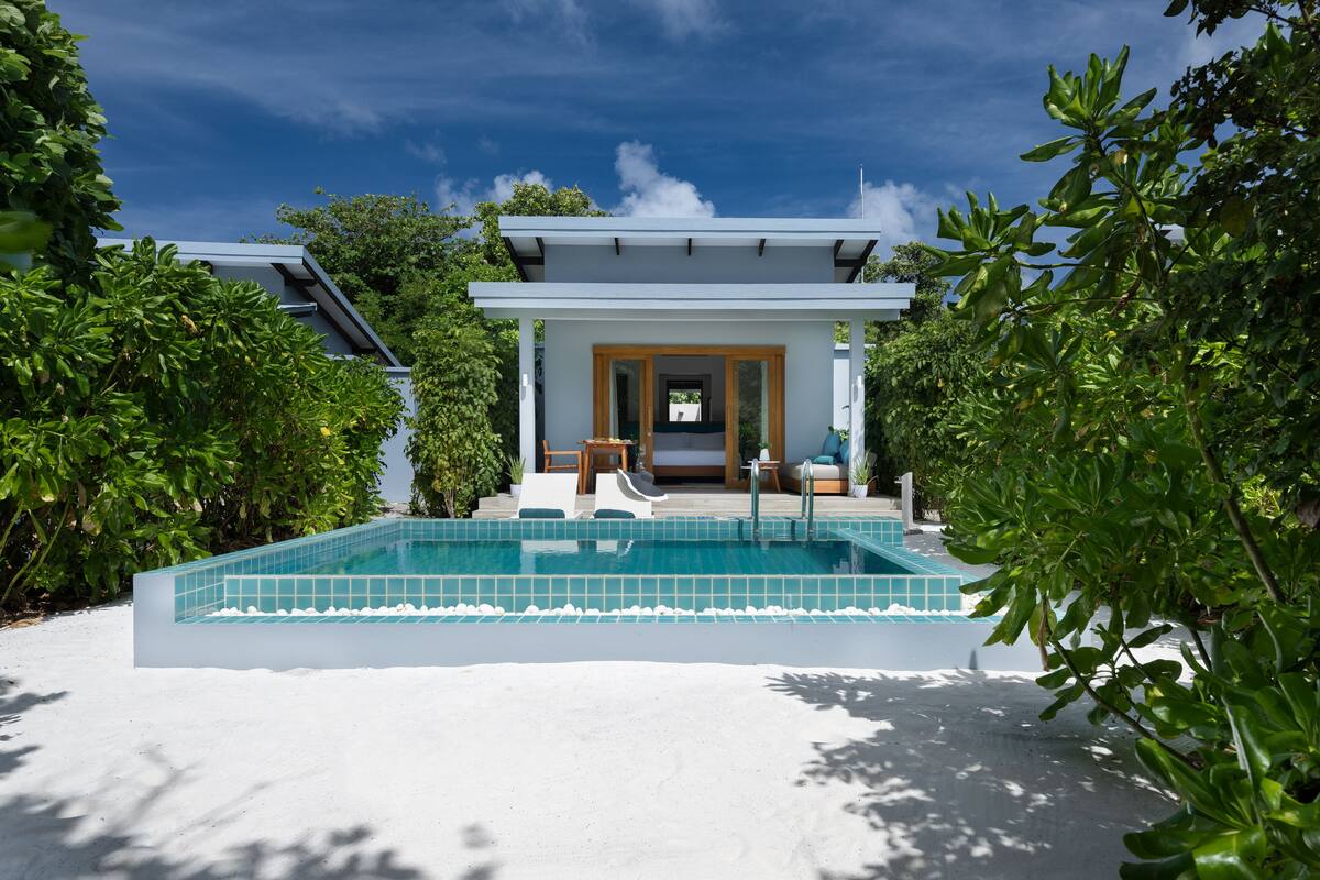 A modern pool area with a clear view of the pool, a covered seating area, and lush greenery surrounding the space.