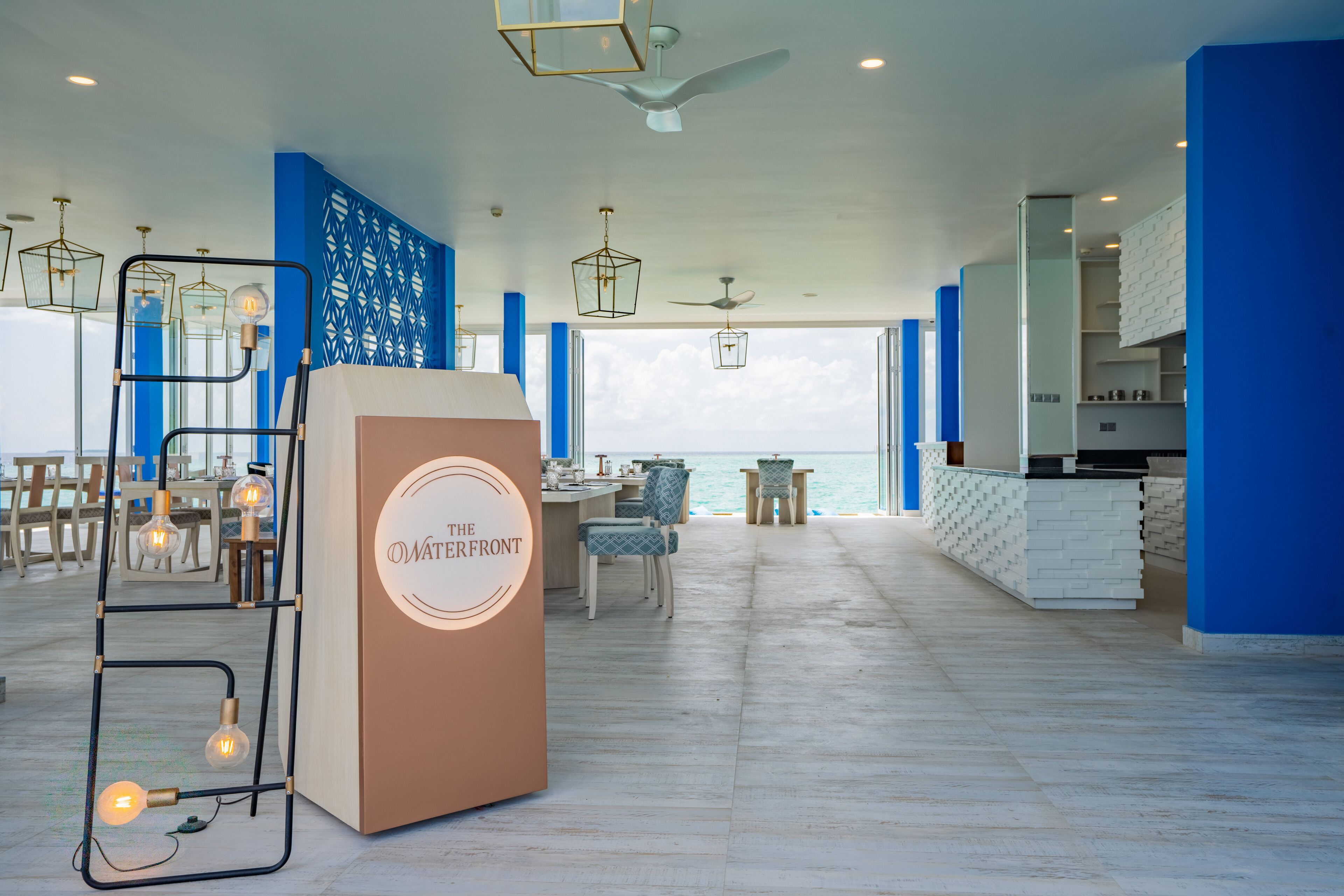 A spacious hotel lobby with a high ceiling, a central seating area, and a view of the sea.