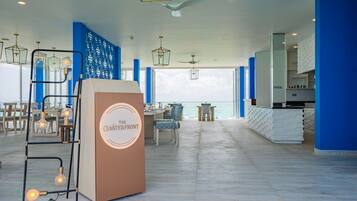 A spacious hotel lobby with a high ceiling, a central seating area, and a view of the sea.