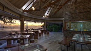 A spacious restaurant with wooden tables and benches, large windows offering a view of palm trees and a sunset, and a stone accent wall. -  Ifuru Island Maldives  (Ifuru)