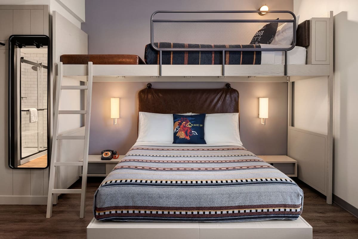 A bunk bed room with a ladder, bedside table, and wall-mounted light fixtures.