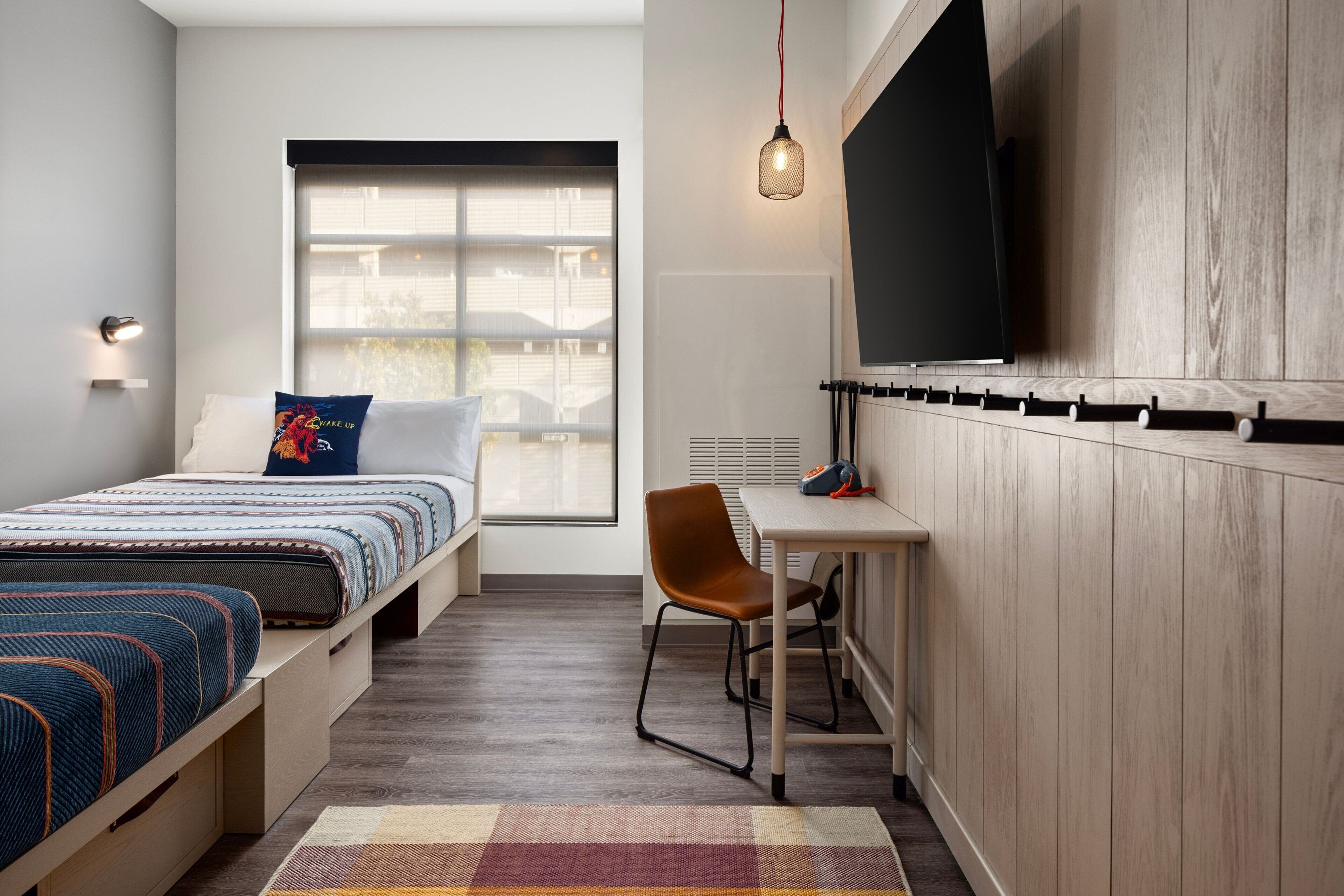 Ein modernes Schlafzimmer mit einem Bett, einem Schreibtisch, einem Stuhl, einem Fernseher und einem Fenster.