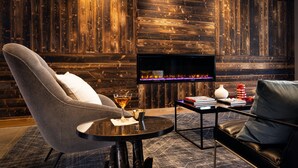 A modern living room with a fireplace, a grey armchair, a black leather sofa, and a small table with books and a glass. - Moxy Omaha Downtown (Omaha)