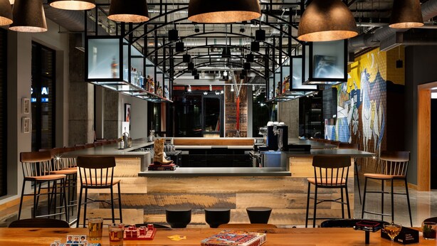 A modern bar area with high ceilings, pendant lighting, and a central bar counter. - Moxy Omaha Downtown (Omaha)