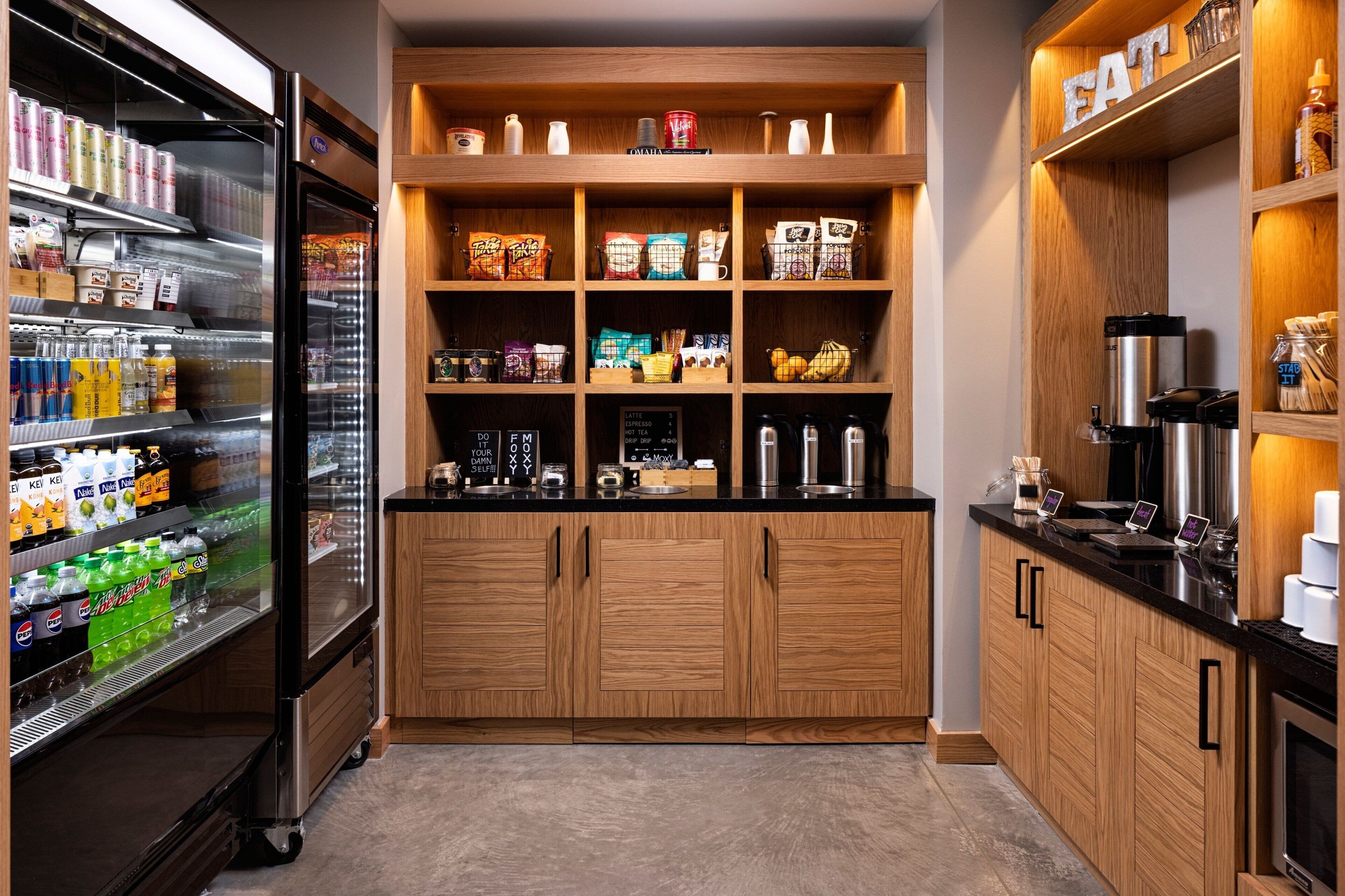 A kitchen with wooden cabinets, a refrigerator stocked with beverages, and a coffee station.