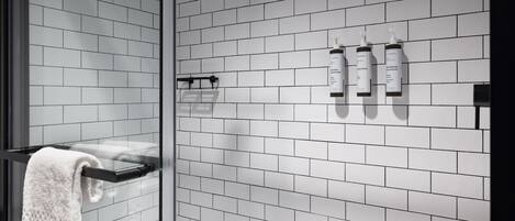 A bathroom with white subway tiles, a glass shower enclosure, and toiletries on the wall.