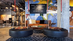 A modern lounge area with a mural, a seating area with tire swings, and a digital display board. - Moxy Omaha Downtown (Omaha)
