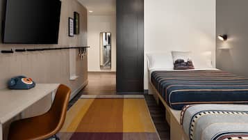 Une chambre d’hôtel moderne dotée d’une télévision à écran plat, d’un bureau avec un téléphone d’époque, d’un grand lit avec une literie à motifs et d’un tapis coloré.