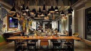 A modern dining area with a long wooden table, multiple chairs, and hanging pendant lights. - Moxy Omaha Downtown (Omaha)