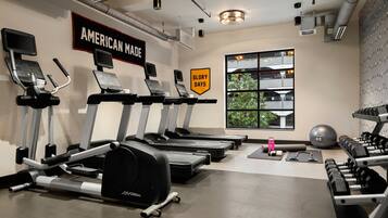 A gym with treadmills, dumbbells, and a large window with a view of trees.