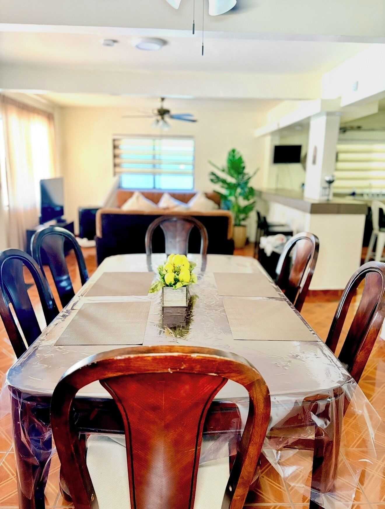 Un comedor con una mesa dispuesta para seis personas, rodeada de sillas, un ventilador de techo y vista al salón.