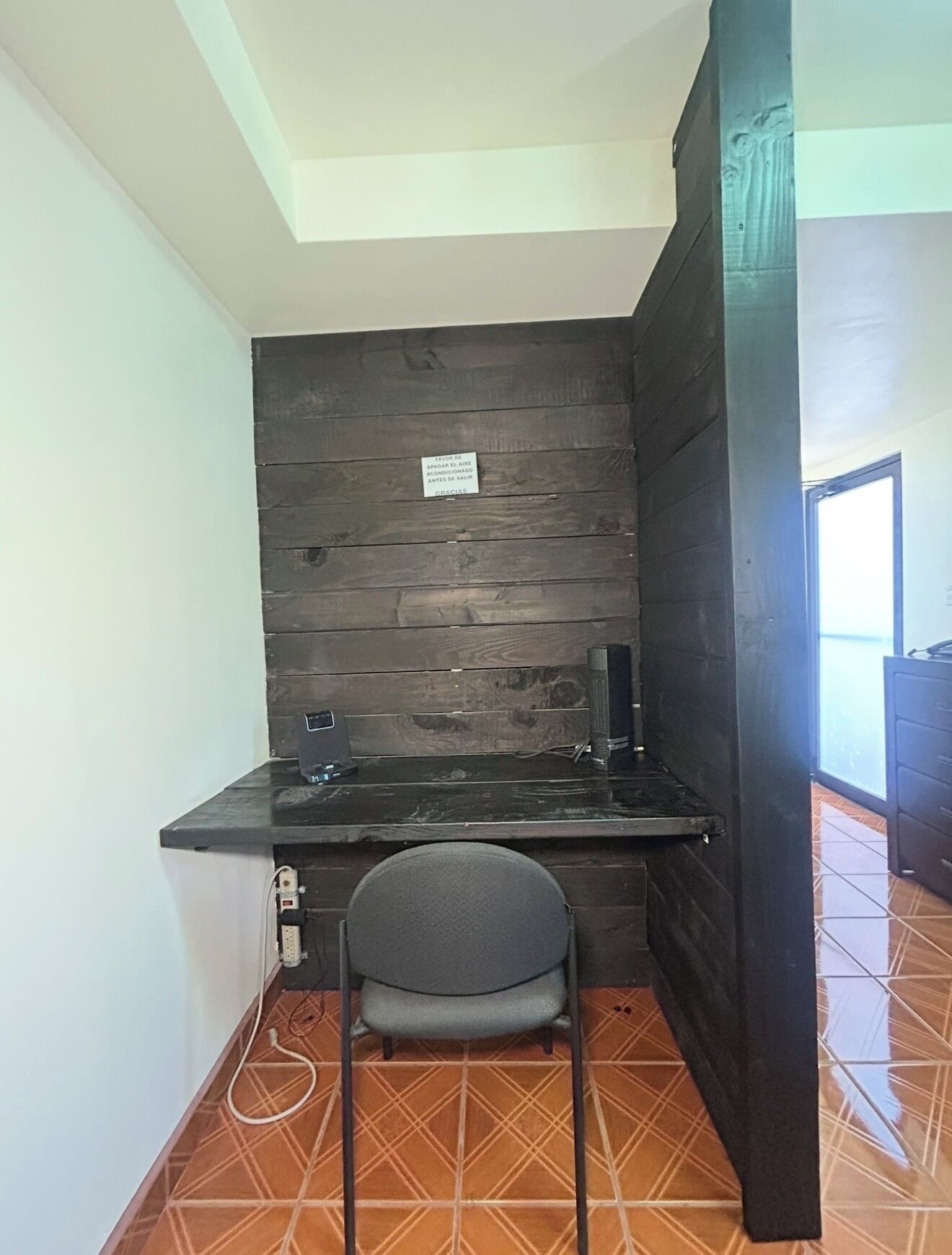 Une petite pièce avec un mur d’accent en bois foncé, une seule chaise, une petite table et une fenêtre.