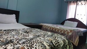 Una habitación con cama, mesita de noche y escritorio. Hay una ventana con cortinas.
