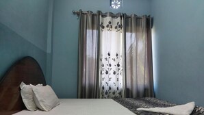 Un dormitorio con cama, cabecera, ventana con cortinas y un tragaluz pequeño.