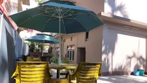 Un patio con una mesa, dos sillas, una sombrilla verde y una pared con un mural.