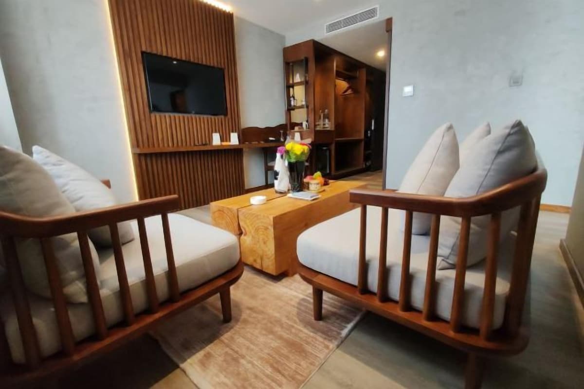 Una sala de estar moderna con dos sillones de madera, una mesa de centro de madera y un televisor montado en una pared de paneles de madera.
