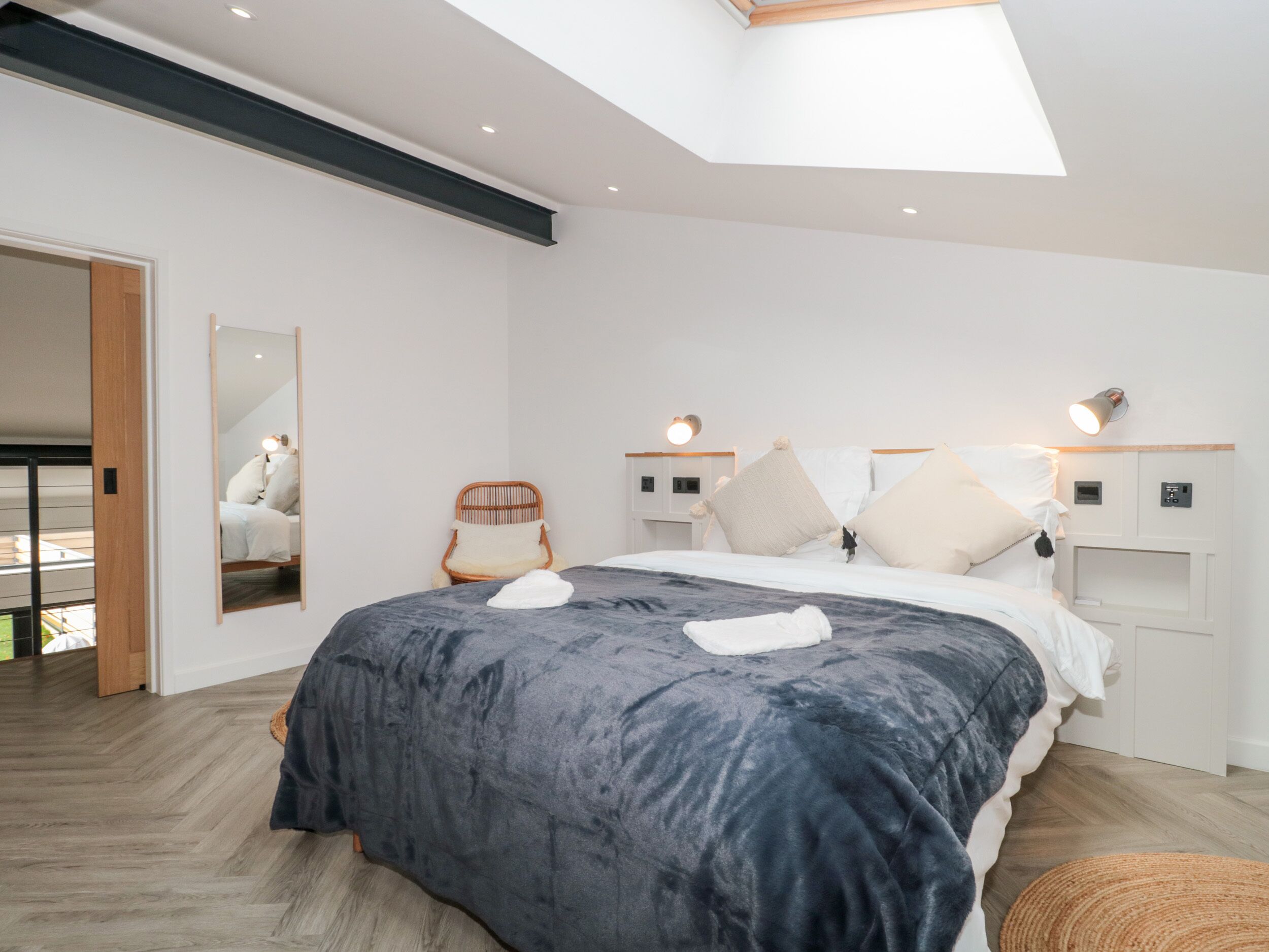 Een moderne slaapkamer met een groot bed, dakraam, een stoel en nachtkastjes met lampen.