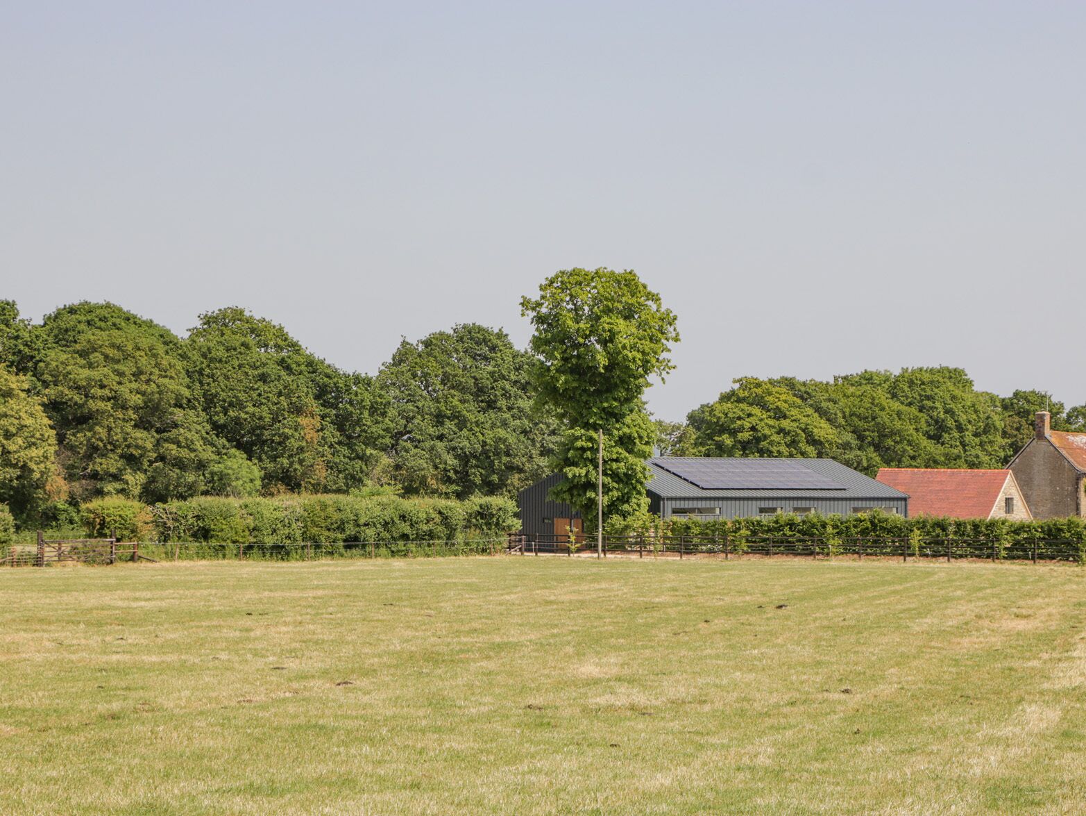 A rural landscape with a large open field, a building with a metal roof, and dense trees in the background.