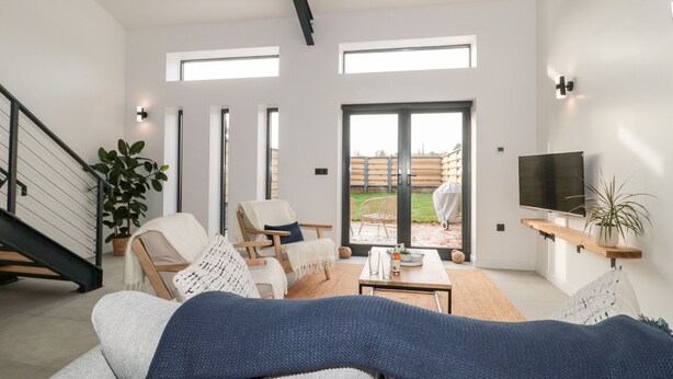 A modern living room with a sofa, chairs, a coffee table, a TV, and a staircase. - Linden Barn (Okehampton)