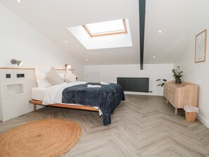 Une chambre à coucher moderne avec une lucarne, un lit recouvert d’une couverture bleu foncé, une commode en bois et un radiateur.