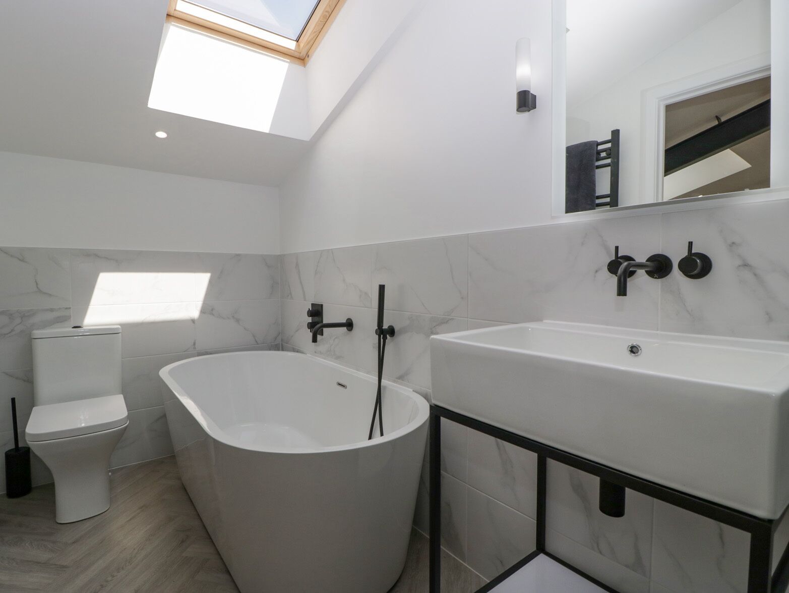 A modern bathroom with a skylight, a freestanding bathtub, a toilet, and a vanity with a mirror.