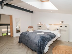 Une chambre moderne avec une lucarne, un lit recouvert d’une couette grise, une chaise en bois et une table de chevet avec une lampe.