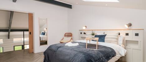 Un dormitorio moderno con tragaluz, una cama con manta oscura, una mesita de noche con planta y una silla.