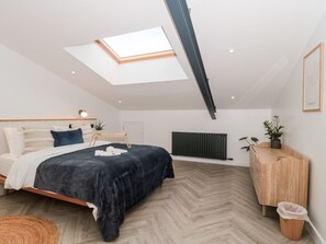 Une chambre moderne avec un puits de lumière, un lit recouvert d’une couverture foncée, une table de chevet en bois, un radiateur et une armoire en bois.
