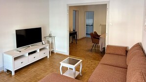Una sala moderna con un sofá grande, un televisor de pantalla plana y una zona de comedor con sillas y una mesa.