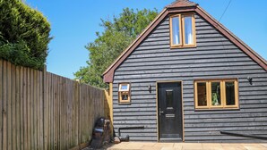 A small, single-story wooden house with a dark gray exterior and a brown roof. It features a front door with a window above it, a small window on the right side, and a mailbox on the left. - Foxes Earth (Salisbury)