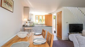 A dining area with a wooden table set for four, a kitchen in the background, and a staircase leading to another level. - Foxes Earth (Salisbury)