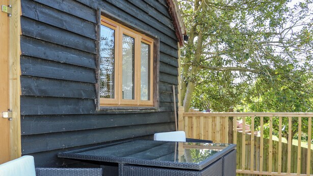 A wooden cabin with a glass table and wicker chairs on a deck. - Foxes Earth (Salisbury)