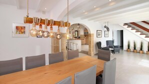 A spacious dining area with a wooden table and chairs, a kitchen in the background, and a staircase leading to an upper level. - Villa Sa Mola, a splendid majorcan house located in a privileged enclave. (Cala San Vicente)