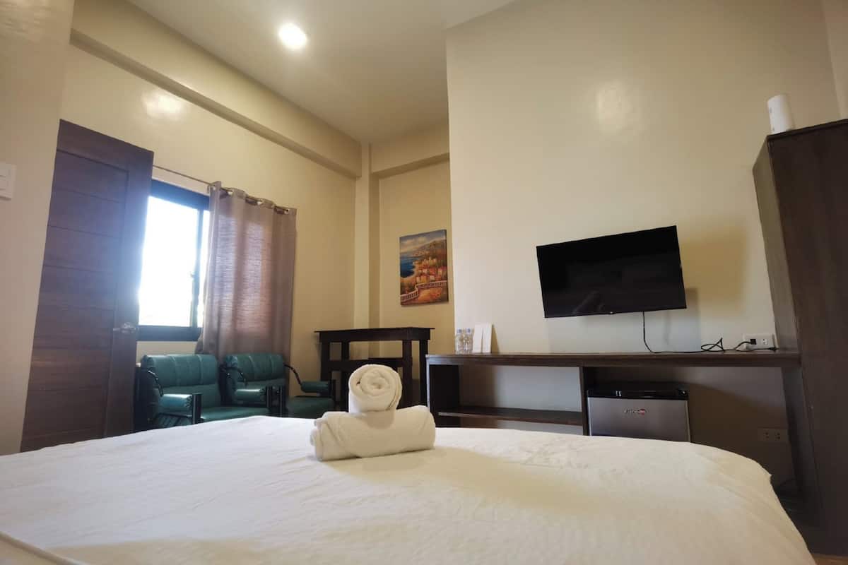 Ein Hotelzimmer mit Bett, Schreibtisch, Fernseher und einer kleinen Küchenzeile.