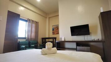 A hotel room with a bed, a desk, a television, and a small kitchenette.