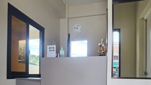 Quarto com piso de madeira, divisória branca, relógio na parede e janela com vista para o exterior.