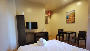 Quarto de hotel com cama, escrivaninha, cadeira, televisão e um quadro na parede.