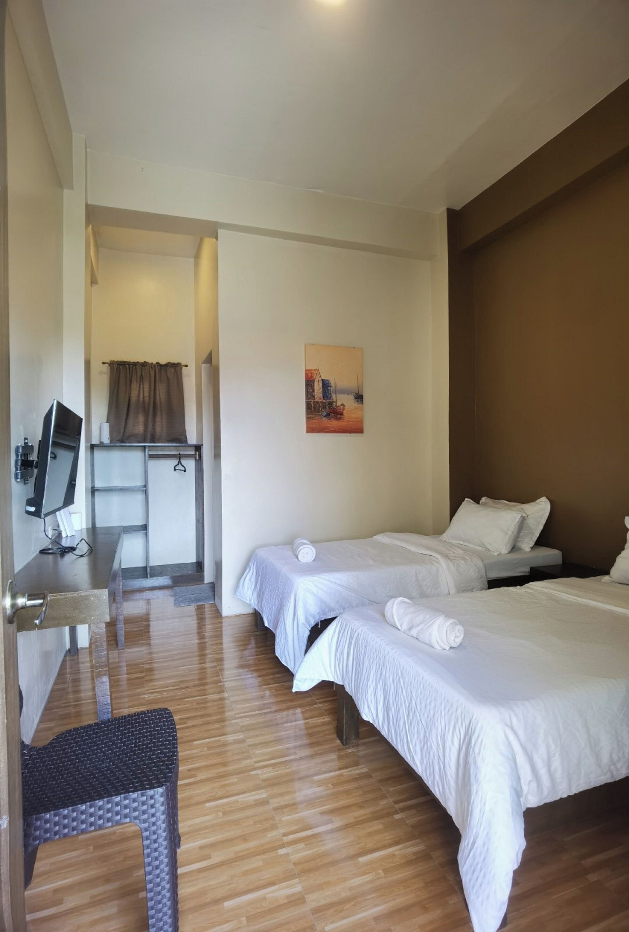 A hotel room with two beds, a desk with a computer, a chair, and a painting on the wall.