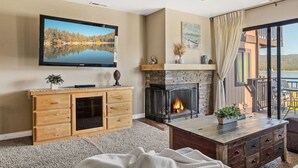 Ein Wohnzimmer mit Kamin, einem an der Wand befestigten Fernseher und Blick auf einen See durch das Fenster.